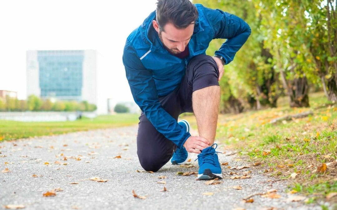 Male runner with ankle pain kneeling down and holding his ankle/