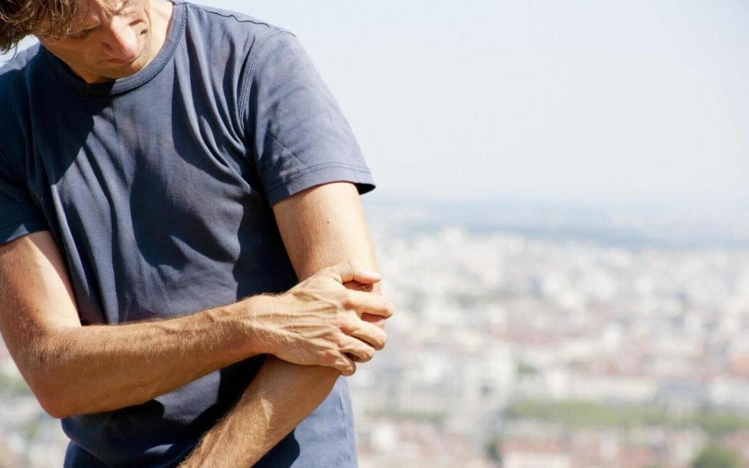 Man experiencing elbow pain clutching his elbow on the lateral side. Tennis elbow.