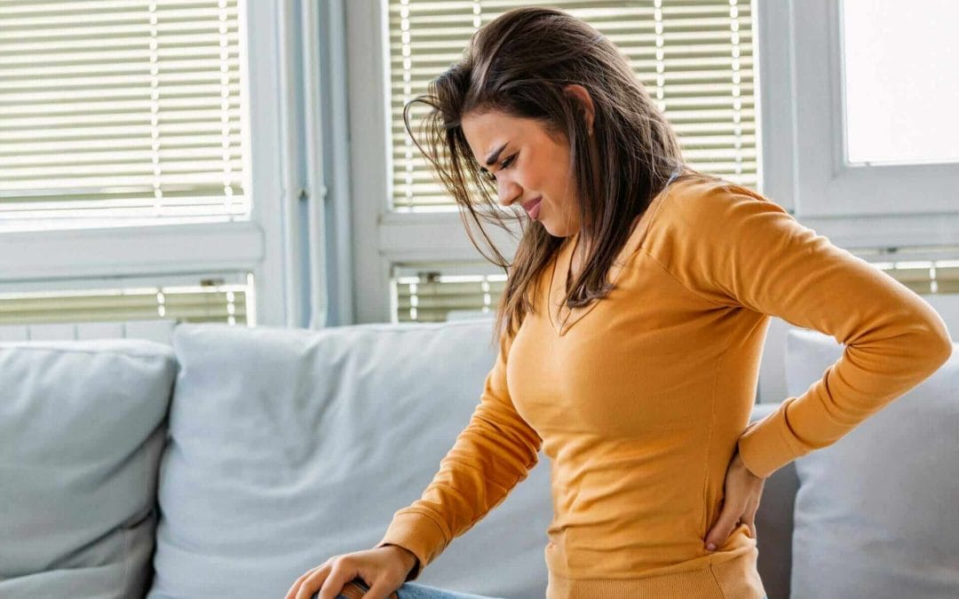 A young woman experiencing low back pain at home.